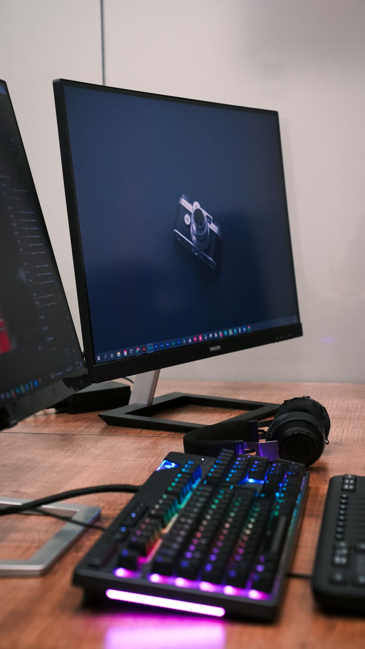 Teclado mecánico retroiluminado y auriculares sobre un escritorio, junto a dos pantallas